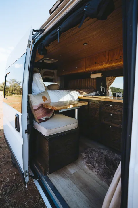 Cozy camper van interior, perfect for your next RV rental! Features a comfortable bed, dining table, and kitchen for travel.. Dodge 1500 2020
