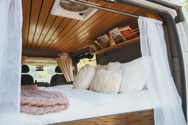 An rv rental's inviting bedroom: plush bed, decorative pillows, wood-paneled ceiling, and book storage.. Dodge 1500 2020