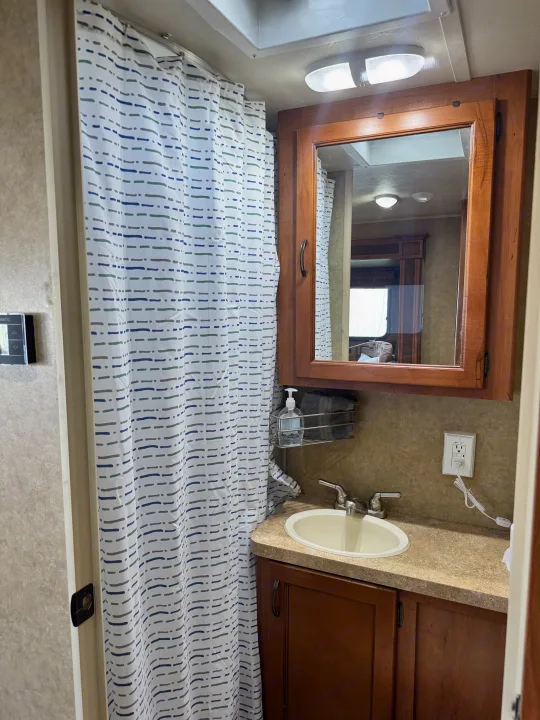 Compact RV rental bathroom: shower with blue/green dash curtain, vanity with sink, mirror cabinet, and overhead lighting.. Forest River Cherokee Grey Wolf 2013