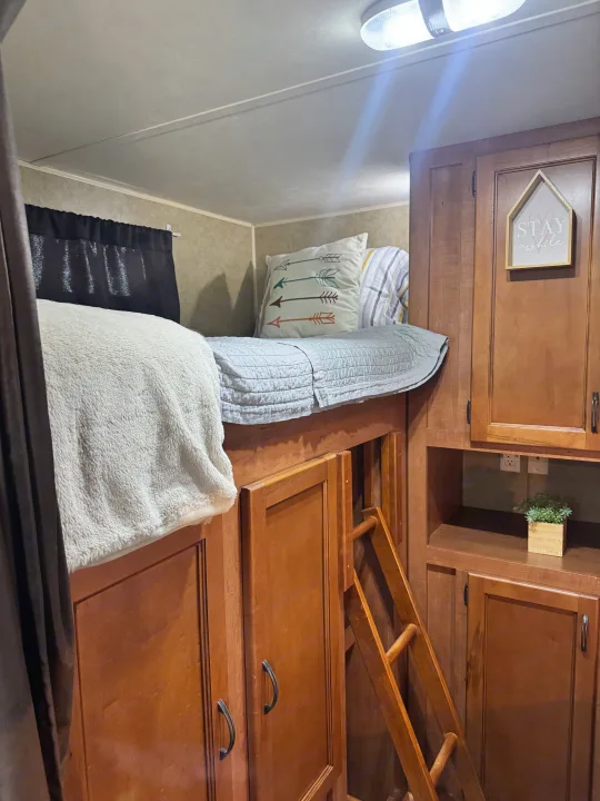 RV rental interior featuring a cozy bunk bed with ladder access, surrounded by wooden cabinetry and storage.. Forest River Cherokee Grey Wolf 2013
