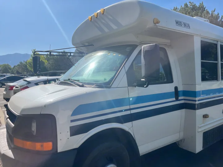 A white commercial bus, identifiable by its 'MID BUS' text and blue stripes, possibly an RV rental, parked outside.. Chevrolet G3500 Express 2006