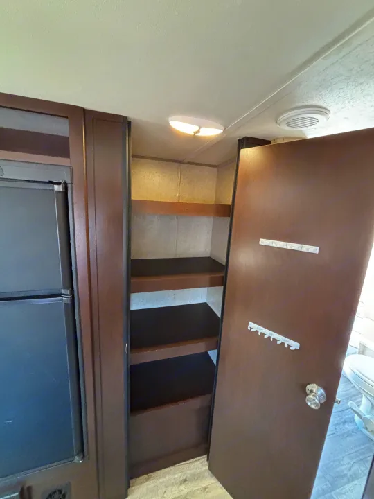 Practical storage in an RV rental: Built-in pantry shelves next to the fridge, with hooks on the adjacent door.. Forest River Cherokee 2017