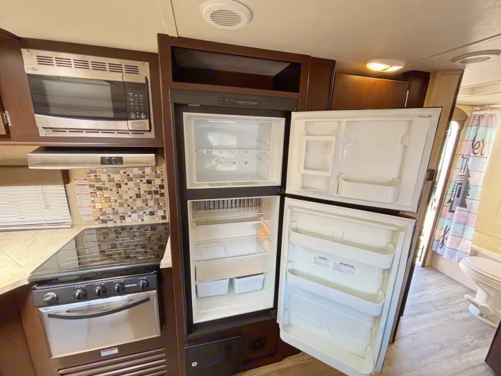 Inside an **rv rental**: A kitchen with stainless microwave, gas range, and open fridge/freezer. Bathroom area with toilet.. Forest River Cherokee 2017