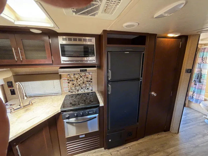 An RV rental's kitchen, featuring a stainless microwave, oven/stove, large Dometic fridge, sink, dark cabinets, and a nearby bathroom.. Forest River Cherokee 2017