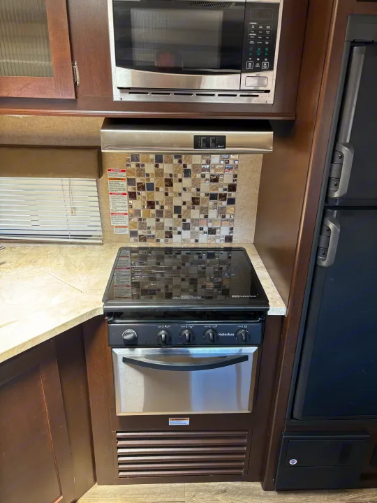 Compact RV rental kitchen setup with a microwave, Suburban stove/oven, and fridge, plus safety warnings for campers.. Forest River Cherokee 2017