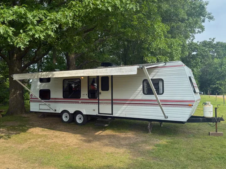 White travel trailer RV rental with extended awning at a shaded campsite.. Jayco 300dbbh 1994
