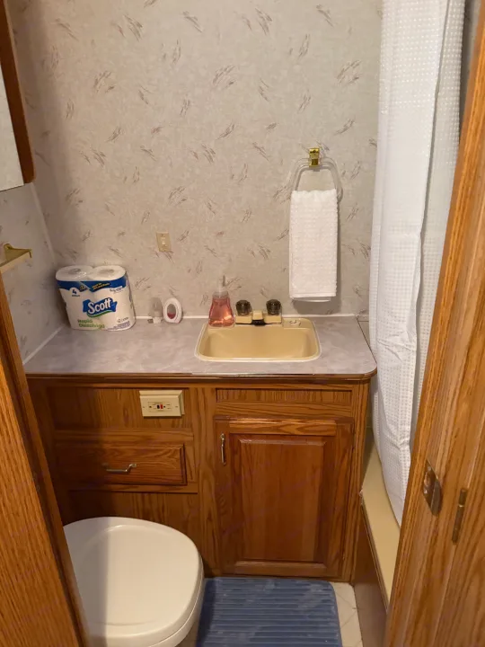 Compact RV rental bathroom showcasing a tan sink, white toilet, wooden cabinets, and a shower. Efficient design for travel.. Jayco 300dbbh 1994