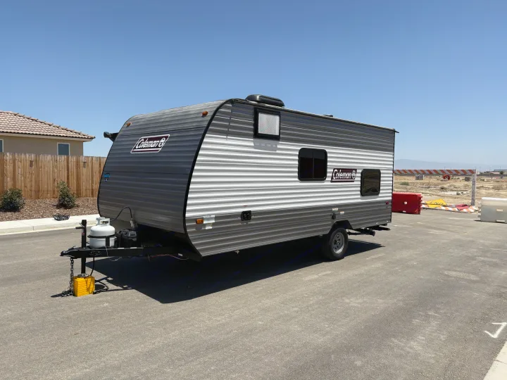 A modern gray and white Coleman travel trailer, ideal for your next RV rental adventure. Parked under a clear sky in a developing area.. Dutchmen Coleman 2024