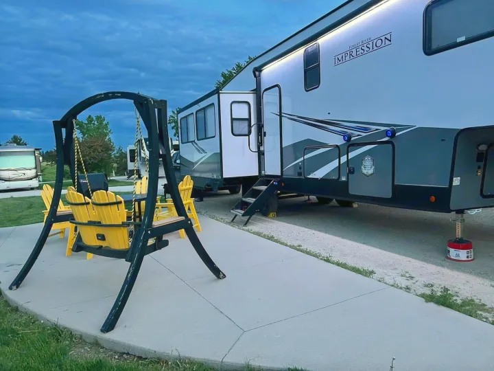 Large RV rental parked at a site, with a patio swing and yellow chairs ready for outdoor relaxation. Ideal camping.. Forest River Impression 2022