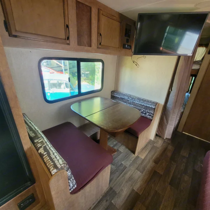 View of an RV rental interior featuring a cozy dinette with rich wood-look flooring, overhead cabinets, and a mounted TV.. Starcraft Launch Ultra Lite 2018
