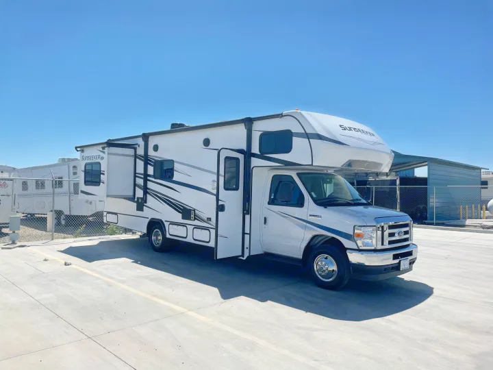 Bright white Sunseeker RV rental with an extended slide-out, parked on a sunlit concrete lot under a blue sky.. Forest River Sunseeker 2022