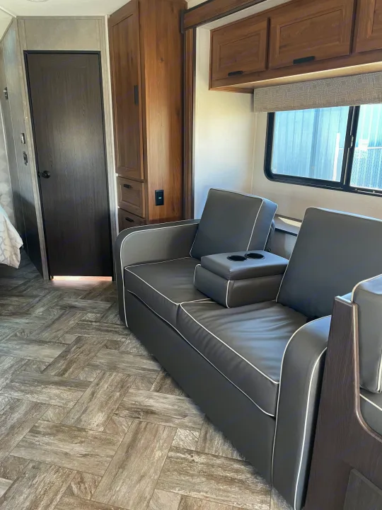 Modern RV rental interior: cozy gray sofa with cupholders, wood-tone cabinets, and stylish wood-look flooring.. Forest River Sunseeker 2022