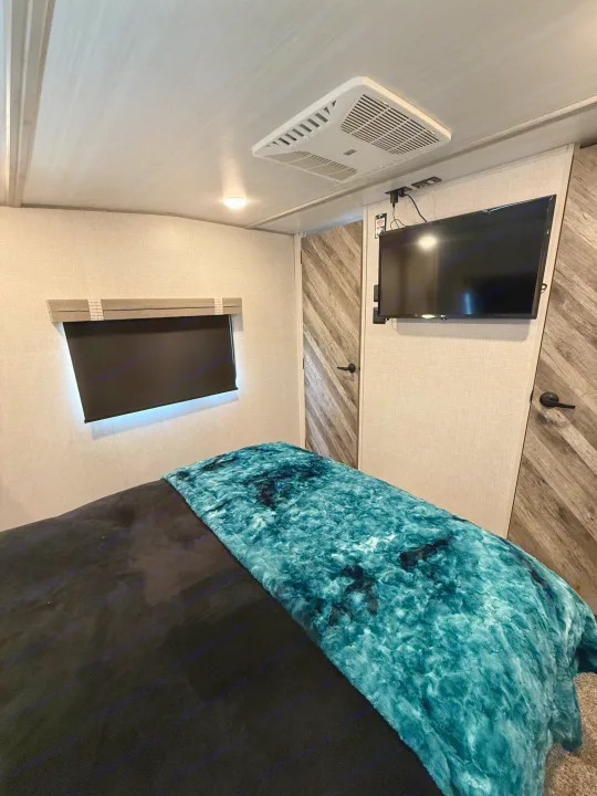 Cozy RV bedroom interior with a teal blanket, window, TV, and AC unit. Perfect for your next RV rental adventure.. Forest River Impression 2022