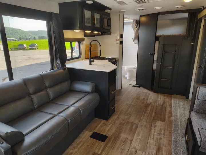 Spacious RV rental interior features a black leather sofa, full kitchen, bathroom, and bunk beds with scenic views.. Forest River Patriot 274BRB 2022