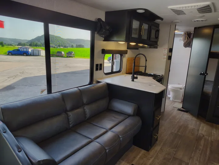 Inside a stylish RV rental: a comfortable leather sofa, modern kitchen, and mountain view from the large window.. Forest River Patriot 274BRB 2022
