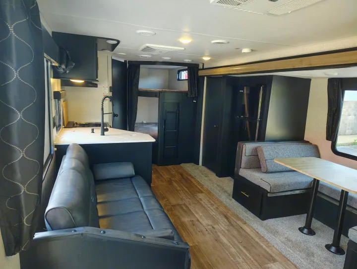 Modern RV rental interior with dark cabinetry, featuring a compact kitchen, dinette, and bunk beds.. Forest River Patriot 274BRB 2022