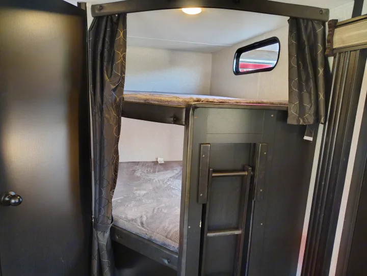Cozy RV rental bunk beds, perfect for family adventures. Features ladder, privacy curtains, and window for light.. Forest River Patriot 274BRB 2022