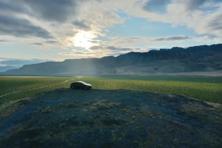 A sleek black car on a hill overlooks a vast green landscape with distant mountains and a dirt road, perfect for an RV rental journey.. Kia EV6 Wind All Wheel Drive 2022