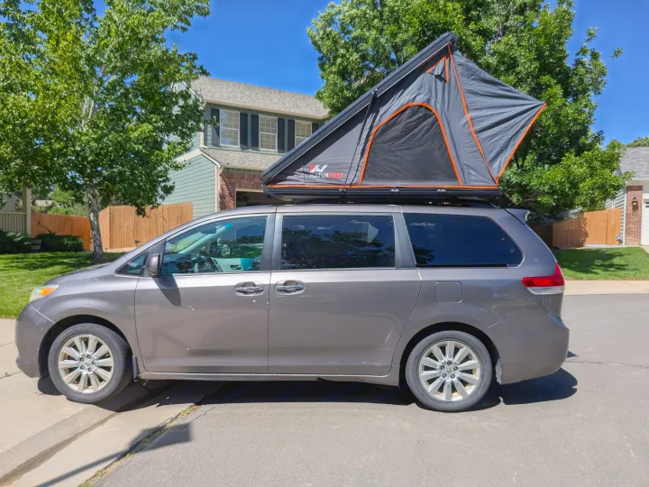 Grey minivan with a grey-orange NaturNest rooftop tent deployed, offering a compact RV rental alternative for outdoor adventures.. Toyota Sienna 2012