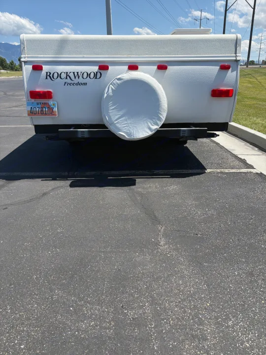Rear view of a white Rockwood Freedom pop-up RV rental camper on asphalt. Features a spare tire and Utah plate.. Rockwood Freedom 2280 BH 2016