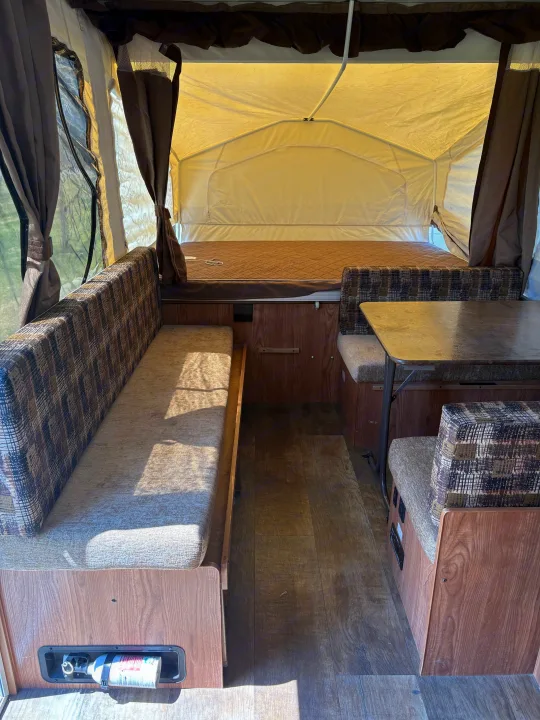 Interior of an RV rental pop-up camper, showing bench seating, a dinette with table, and a rear bed area.. Rockwood Freedom 2280 BH 2016