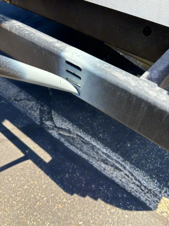 Close-up of an RV rental's metal frame/chassis, showing a support bar slotted into its structure. Dust and shadows are visible.. Rockwood Freedom 2280 BH 2016