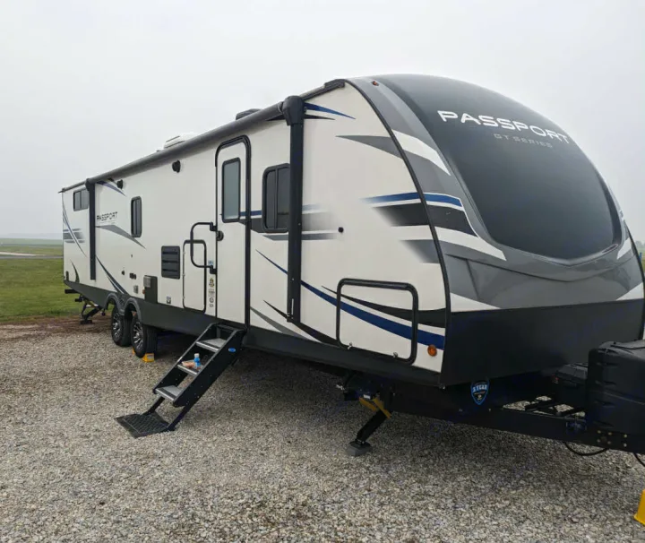 RV rental: A white and grey Passport GT Series travel trailer camper parked on a gravel lot with steps.. Keystone RV 3400QD 2020