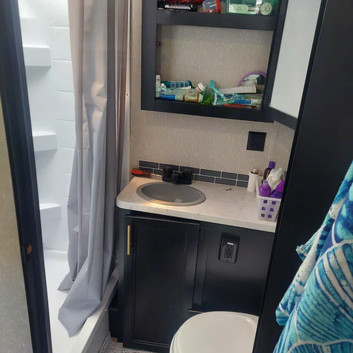 Inside an RV rental: a modern, compact bathroom with a shower, sink, toilet, and ample cabinet storage.. Forest River Grey Wolf Limited 2022