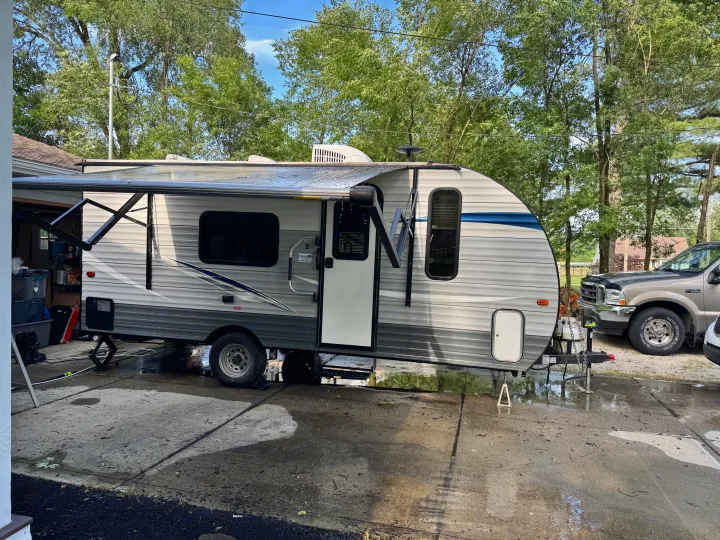 An RV rental travel trailer is parked on a wet driveway with its awning extended, ready for adventure.. Gulf Stream Ameri-Lite Super Lite 2019