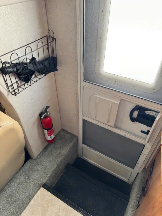 Inside an RV rental: the entry door with screen, steps, and safety features like a fire extinguisher, plus a wall basket.. Coachmen Leprechaun 2001