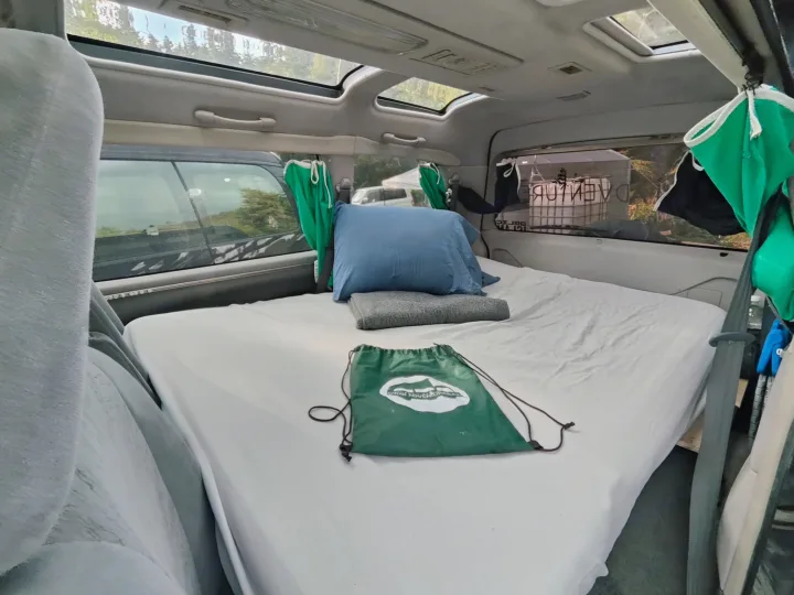RV rental's cozy campervan interior with a comfy bed, blue pillow, green bag, and sunroofs. A perfect sleeping area.. MITSUBISHI Delica 1997