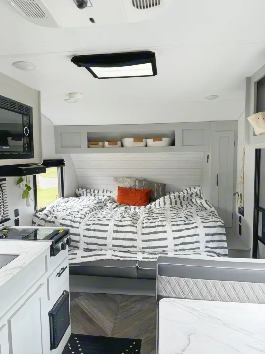 Cozy RV rental interior: modern bedroom with striped bedding, compact kitchen, and dining area.. Forest River Salem FSX 2022