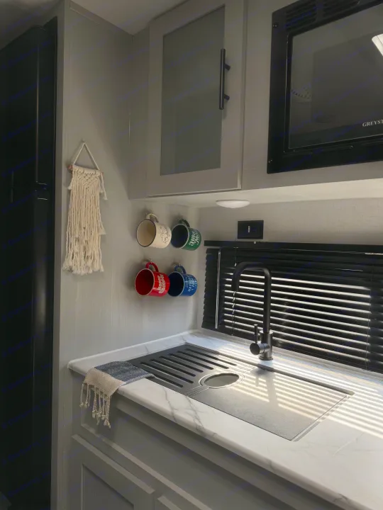 Stylish RV rental kitchen featuring a black sink, microwave, gray cabinets, and sunlight stripes through blinds.. Forest River Salem FSX 2022