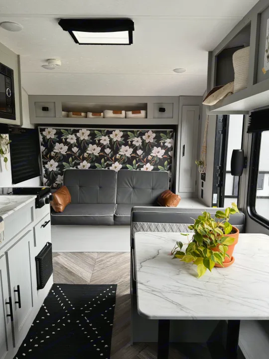 Cozy renovated RV rental interior: A modern mobile living space with gray sofa, floral wall, dining area, and plant. Perfect for travel!. Forest River Salem FSX 2022
