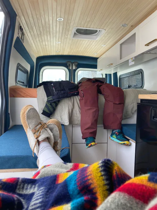 Cozy RV rental interior: feet up with a colorful blanket, winter gear ready, and wooden ceiling.. Ford Transit 2019