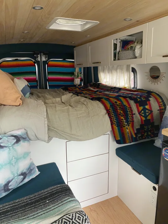 Cozy RV rental interior featuring a comfy bed with colorful blankets, overhead storage, and a wooden ceiling.. Ford Transit 2019