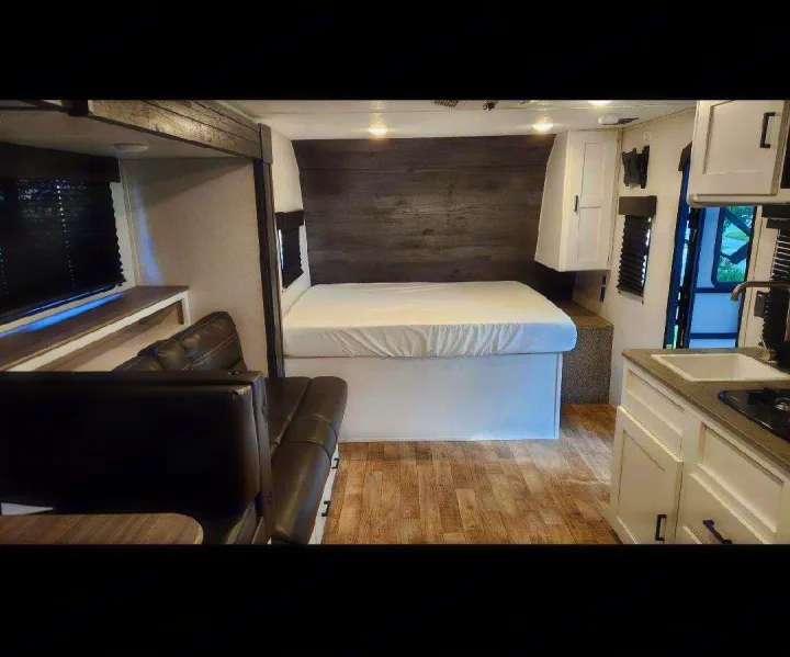 This modern RV rental interior offers a comfy bed, functional kitchen with sink & stovetop, and a cozy dinette area.. Keystone RV Hideout 2021