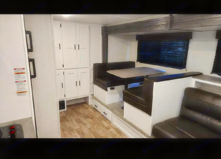 Inside an RV rental: a cozy dinette with dark cushions, white storage cabinets, and wood flooring for comfortable journeys.. Keystone RV Hideout 2021