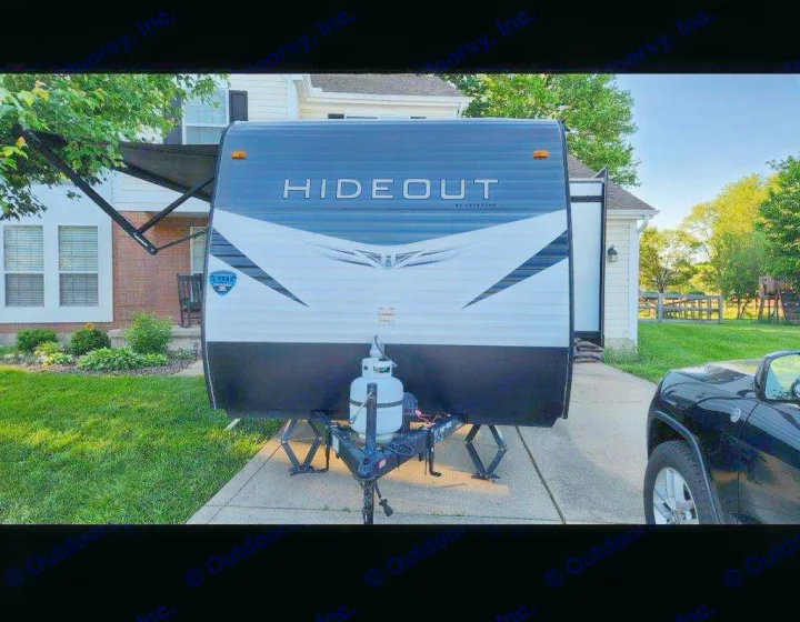 A sleek Hideout travel trailer, ideal for an rv rental, parked in a residential driveway with its awning extended.. Keystone RV Hideout 2021
