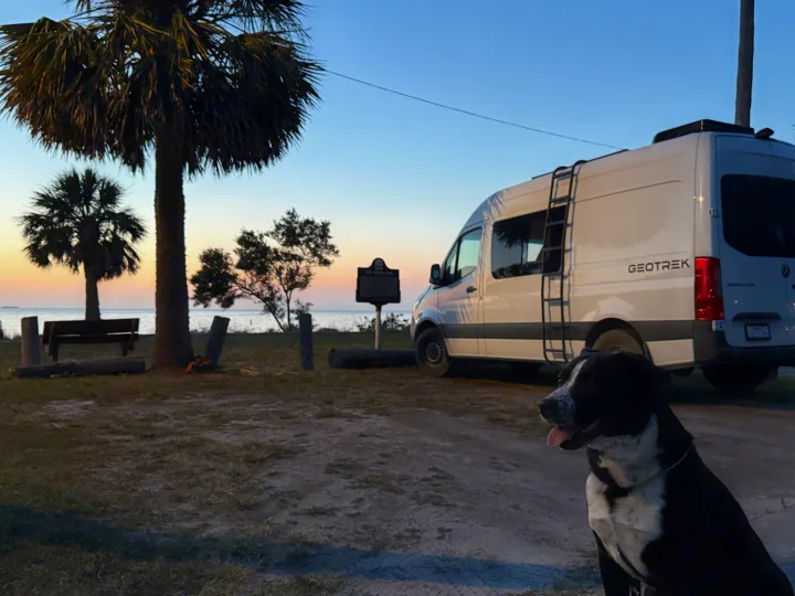 Enjoy an RV rental adventure! A white Geotrek camper van is parked at a scenic waterfront park with a dog at sunset.. Mercedes-Benz Sprinter 2024
