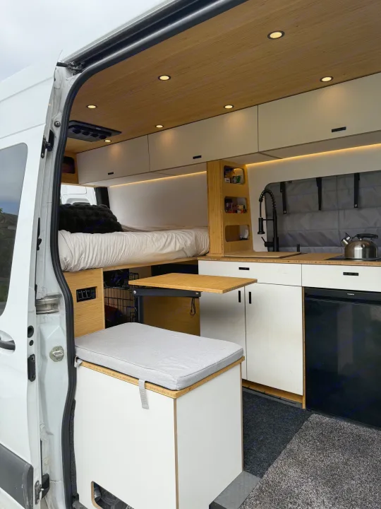This RV rental shows a modern camper van interior with a bed, kitchen, and pull-out table, optimized for comfortable travel.. Mercedes-Benz Sprinter 2024