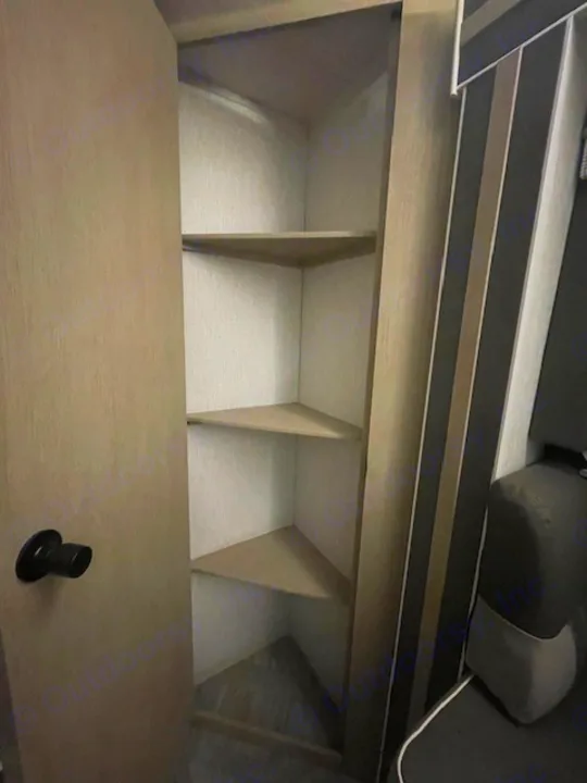 Efficient corner pantry storage in an RV rental, featuring multiple shelves & a door with a black handle.. Forest River Wildwood X-Lite 2023