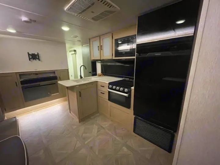 Interior of a modern RV rental, showcasing a compact kitchen with black appliances, fireplace, and living area.. Forest River Wildwood X-Lite 2023