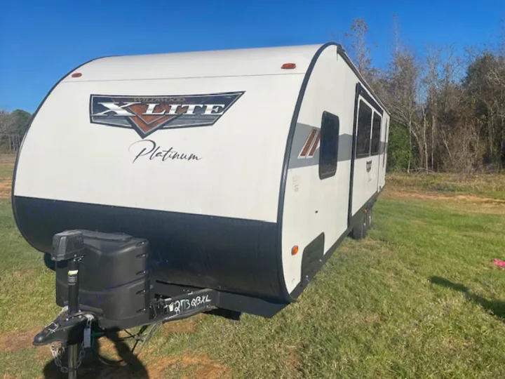 White Wildwood X-Lite Platinum travel trailer, a spacious RV rental, parked on green grass. A bright day for your outdoor escape.. Forest River Wildwood X-Lite 2023