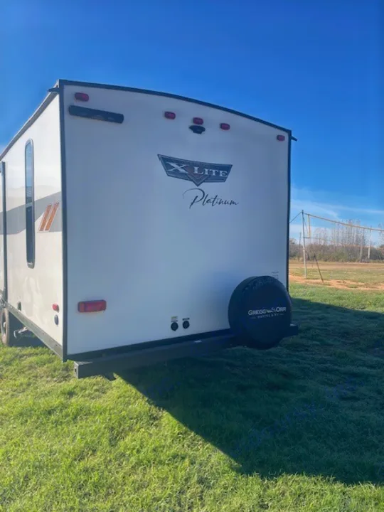 White X-Lite Platinum travel trailer, rear view with spare tire, on green grass under blue sky. Great for your next rv rental.. Forest River Wildwood X-Lite 2023