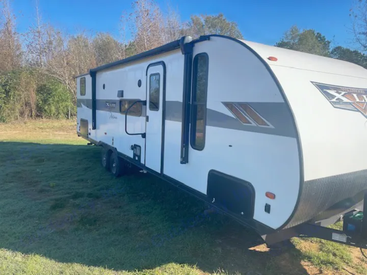 White Wildwood X-Lite travel trailer, an RV rental, parked on green grass under a blue sky.. Forest River Wildwood X-Lite 2023