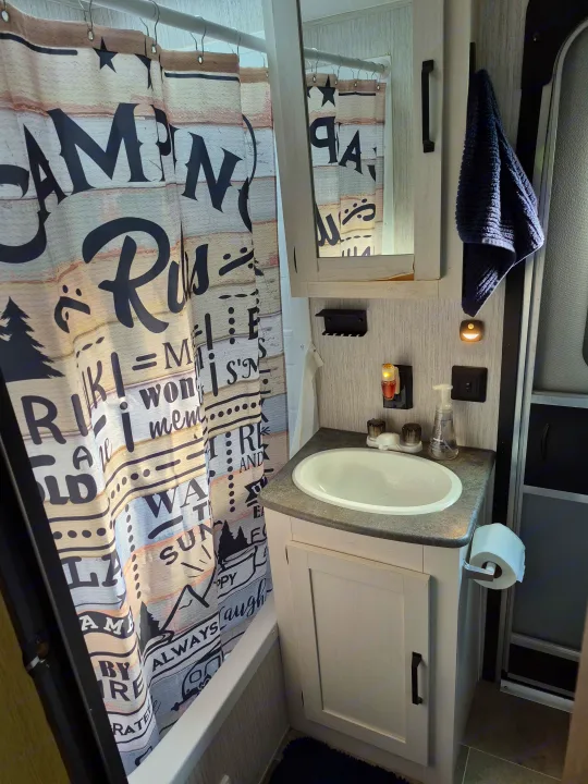 RV rental bathroom features a 'Camping Rules' shower curtain, sink with vanity, and a blue towel. Compact and well-equipped.. Forest River Palomino Puma XLE Lite 2021
