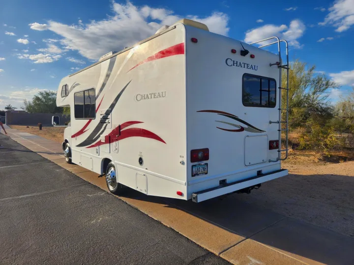 This Chateau RV rental, a white motorhome with red accents, is parked on asphalt in a sunny desert landscape.. Thor Chateau 2013