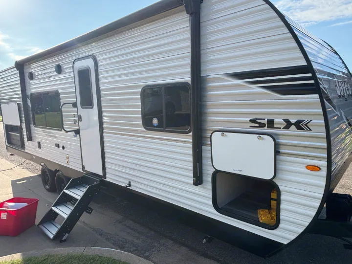 A clean Jayco SLX travel trailer RV rental is parked, showcasing its exterior, deployed steps, and open storage.. Jayco Jay Flight SLX 2025