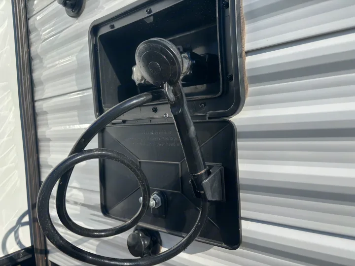 RV rental outdoor shower: Black hose, nozzle, and controls are visible within an open compartment, showing winterization text.. Jayco Jay Flight SLX 2025